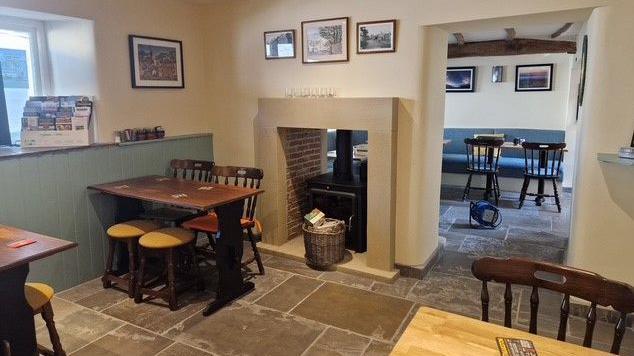 The interior of the pub, which features exposes beams and a log burner, as well as several different tables.