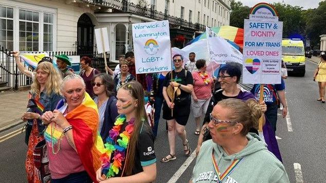 The photos capture lots of women in the parade with colourful face paint on, Pride flags and wooden posters supporting Pride and transgender people. They are walking in the street.
