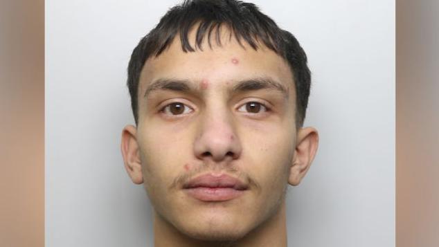 A police mugshot of a 20-year-old man with short dark hair.