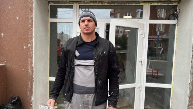 Volodymyr Tsepovatenko, wearing a black jacket and a grey beanie, standing in front of a glass door and windows.
