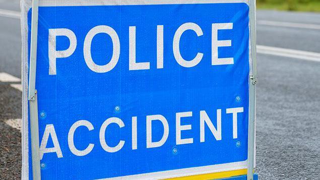 Police accident sign, white writing on blue sign, with a road in the background