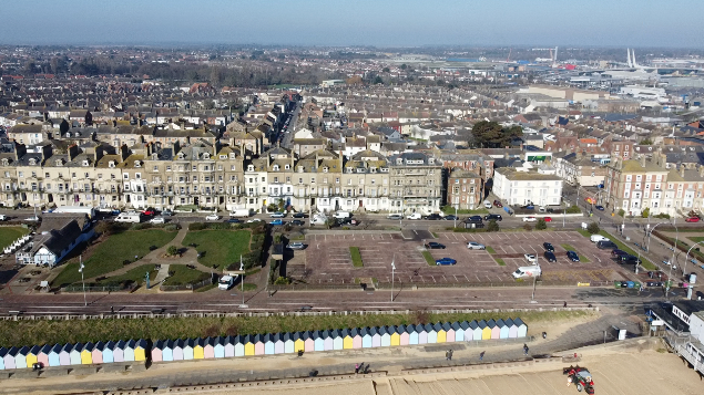 An aerial shot of Lowestoft showing the town in the background and a line of colorful beach huts in the foreground which are in front of a strip of sandy beach