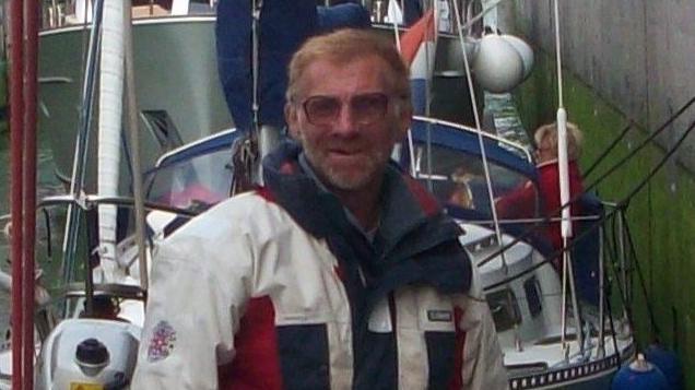 Chris Cowlard wearing a white, red and blue jacket. He is standing in front of two boats.