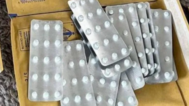 Several silver-coloured blister packs of white pills, lying on top of manilla brown envelopes