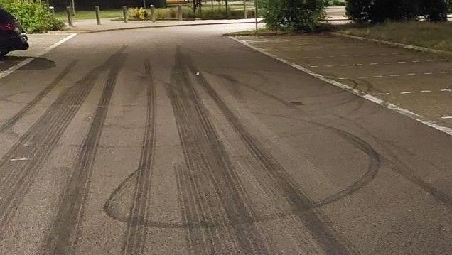 A photo showing a hand holding a fine in a school car park. Tyre marks can be seen on the ground.