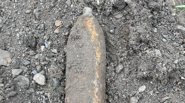 A suspected World War Two bomb encased in dirt and lying on soil and gravel 