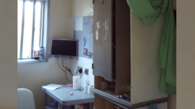 A prison cell with a bed sheet folded up and hanging from the ceiling