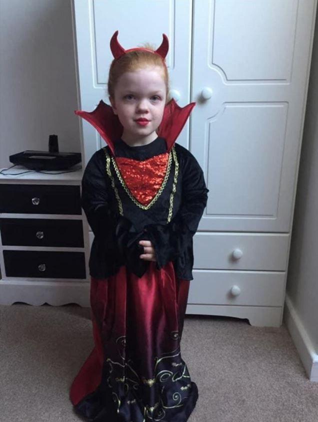 Jessica when she was younger dressed in her Halloween costume. It is a black and red dress. She is wearing red devils horns on her head. 