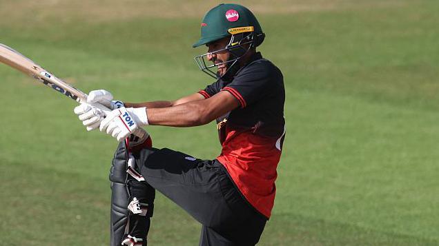 Hamza Shaikh hits a shot for Leicestershire Cricket Club against Kent in the 2025 One-Day Cup while wearing a red and black top, black trousers and a green helmet