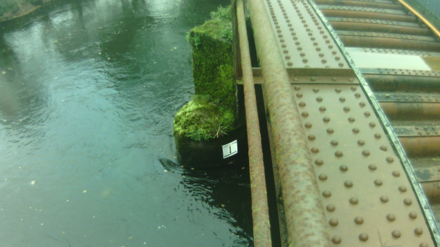 A high water level next to a railway track. There is a white marker on the bridge and the water is below it.