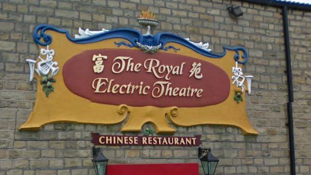 A photo of the cartouche before it fell into disrepair. It reads "The Royal Electric Theatre" in golden letters on a red and yellow background with hints of blue and white.