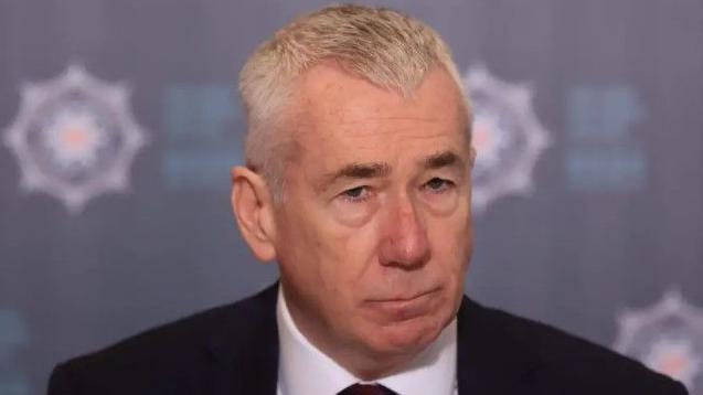 Jon Boutcher. He has white hair, wearing a black blazer, white shirt and dark tie. PSNI signage is in the background.
