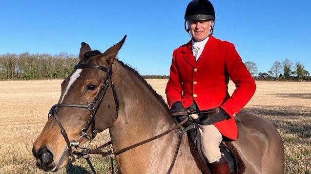 Euan Nicolson, senior master of the Suffolk Hounds wearing a riding hat, white shirt and red jacket sits on his brown horse   