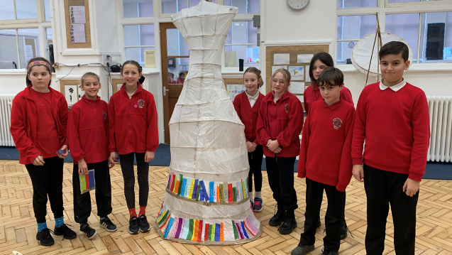 Eight primary school pupils standing around their lantern, which has layers of coloured paper depicting books on shelves