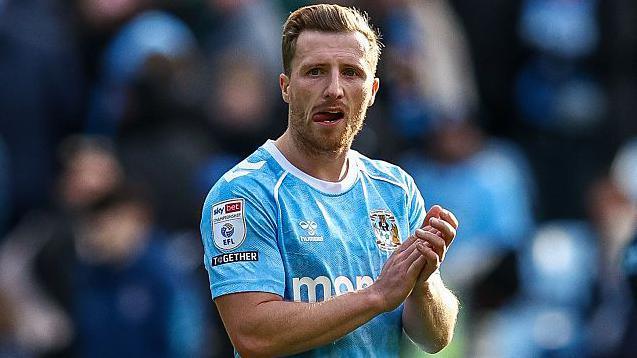 Jamie Allen wears a sky blue and white Coventry City kit and applauds supporters at the end of a match 