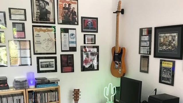 Frames with Rolling Stones magazine covers and other artwork can be seen on white walls. A rock guitar is pinned up in the corner and a shelfcase packed with singles stands beneath