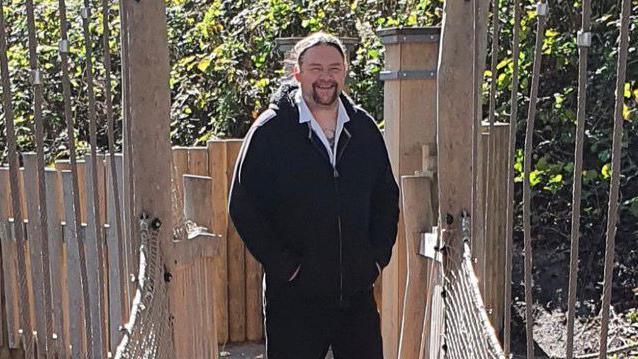 Jimmy Southern standing on a bridge with his hands in his pockets, smiling. 