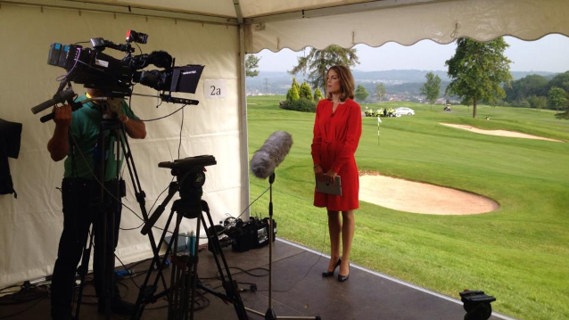 Andrea Byrne wearing a red dress stands in front of a camera and microphone ready to present the ITV Wales news