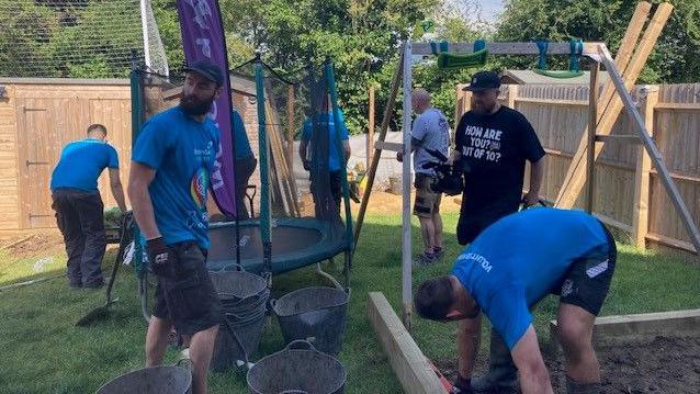 Volunteers in blue uniforms standing on the lawn of a garden, carrying out tasks.