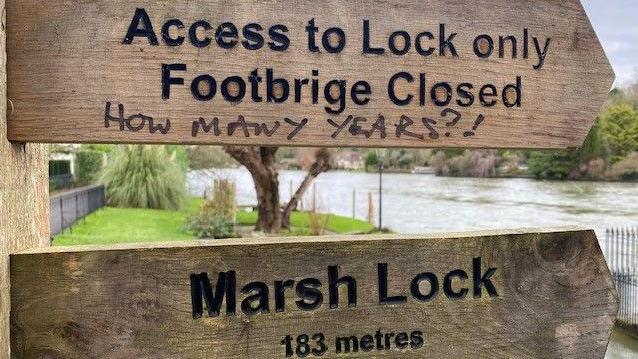 A public footpath sign which reads "Access to Lock only Footbridge Closed."
underneath a member of the public has scribbled How Many Years?!