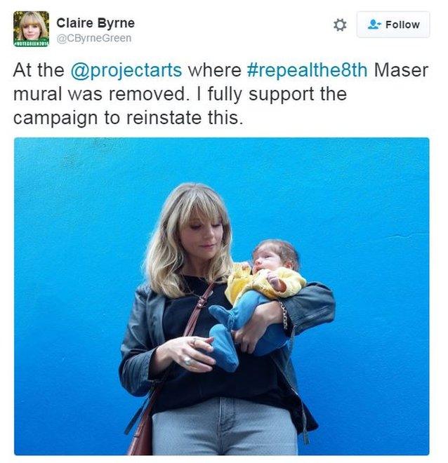 Green Party councillor posing with her baby at painted over wall asking for mural to be reinstated