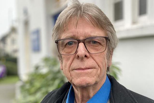 Kelvin Pratt standing outside the white BBC Essex building, wearing a blue collared shirt and black coat. He has glasses and is looking at the camera.
