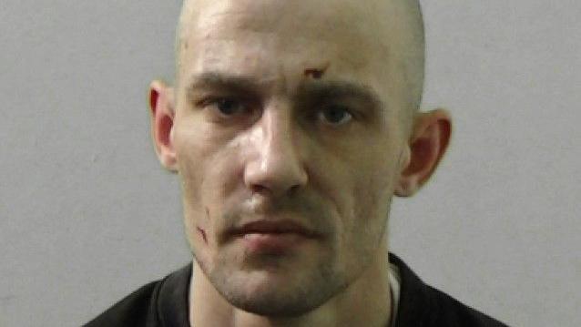 Mugshot of Cullen. He is bald with a very faint grey beard and cuts above his left eye and on his right cheek.