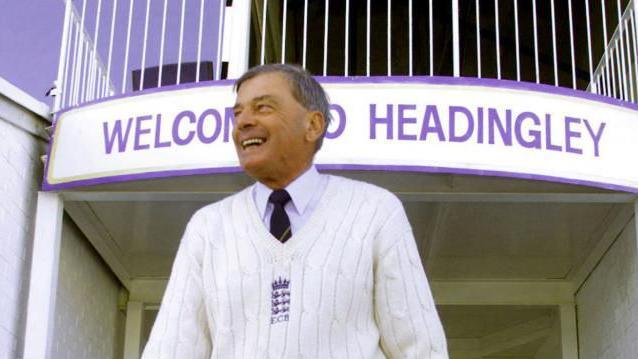Veteran cricket umpire Harold "Dickie" Bird walks onto the pitch at Headingley in Leeds before umpiring his last ever cricket match between Yorkshire and Warwickshire September 13. He is wearing a white sweater with an emblem, a collared shirt, and dark pants stands in front of a building entrance with a sign that reads 'WELCOME TO HEADINGLEY.'