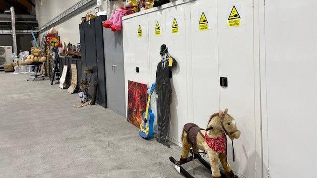 A rocking horse, a guitar and a large life-size cut out of Charlie Chaplin sit in the warehouse with other items 