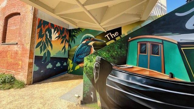 A large mural showing a kingfisher and a narrowboat on walls beneath a bridge