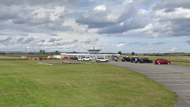 Cars parked near an aviation tower, which is surrounded by green grass. 