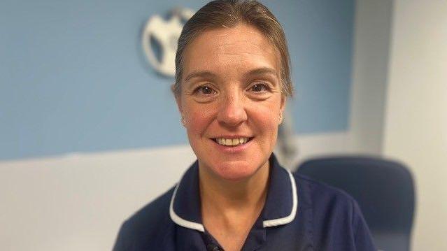 Female nurse in a blue uniform standing within a clinical room at the new Community Diagnostic Centre in Hull. She is staring into the camera and smiling.