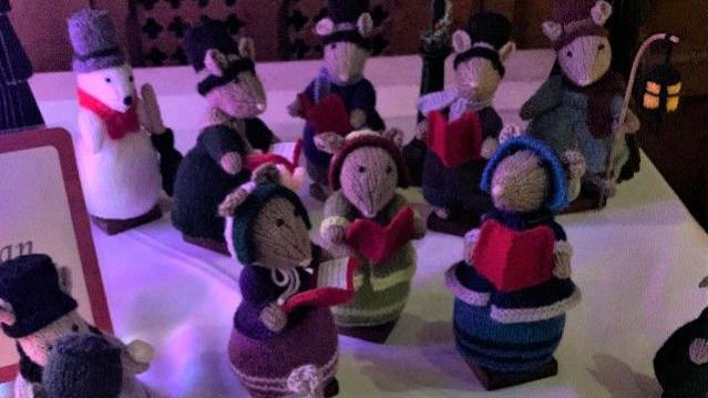 A collection of hand-made mice Christmas carollers. 
Several mice are wearing bonnets and holding carol books. 