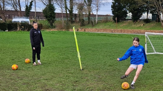 Natasha Allen-Wyatt looks on as a young girl player kicks a ball on a football pitch