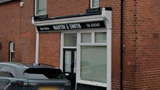 The front of Martin & Smith Bakery which has been painted in black and white. A black car is parked in front of the building.