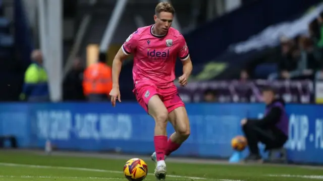 Torbjorn Heggem carries the ball out from defence while playing in a match for West Bromwich Albion and wearing a pink away kit.