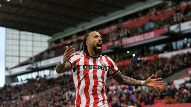 Sorba Thomas cheering in a red and white striped Stoke City home shirt with the crowd behind him