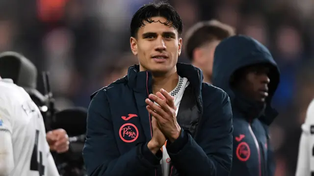 Marko Stamenic claps wearing a navy jacket over his Swansea kit