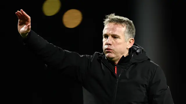 Wrexham manager Phil Parkinson in a black coat with his hand in the air