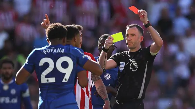 A Chelsea player is sent off by a referee who brandishes a red card