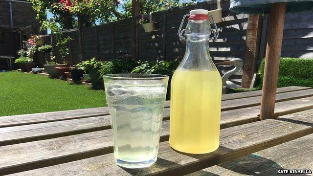 a cold drink on a table with a bottle of cordial next to it.