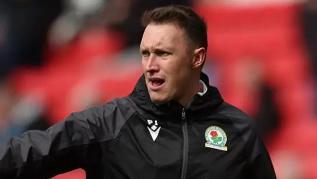 Phil Jones, in a black Blackburn Rovers training top, points from the sidelines during a match.