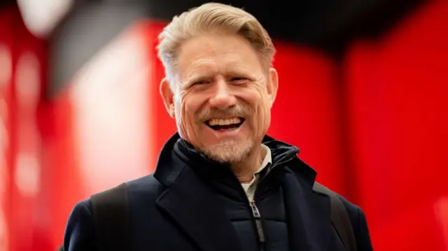 A smiling Peter Schmeichel wearing a dark jacket