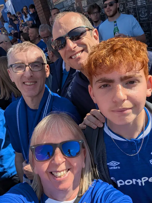 A woman takes a selfie with a group of three men. All of the group are dressed in Everton memorabilia