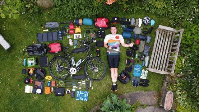 Simon Watts laying down in a garden surrounded by various items laid out next to his bike.
