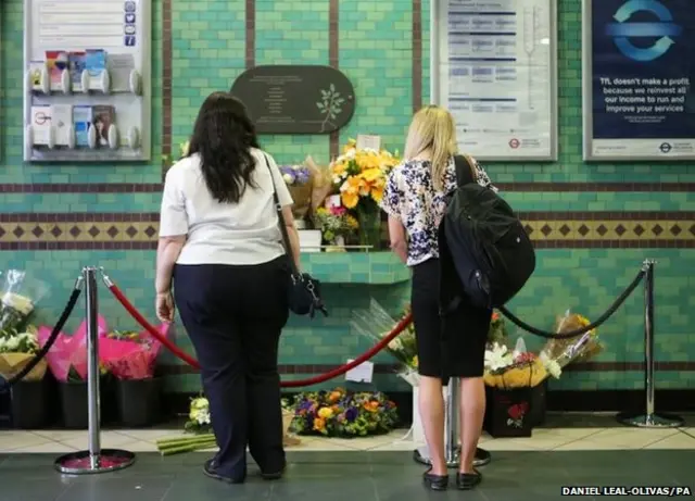 People look at flowers left by the July 7 memorial plaque at Aldgate Station, London