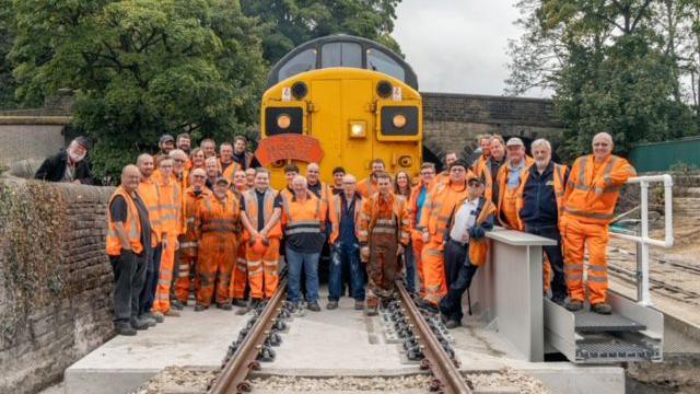 A group of 35 volunteers in orange overalls standing in front of a train