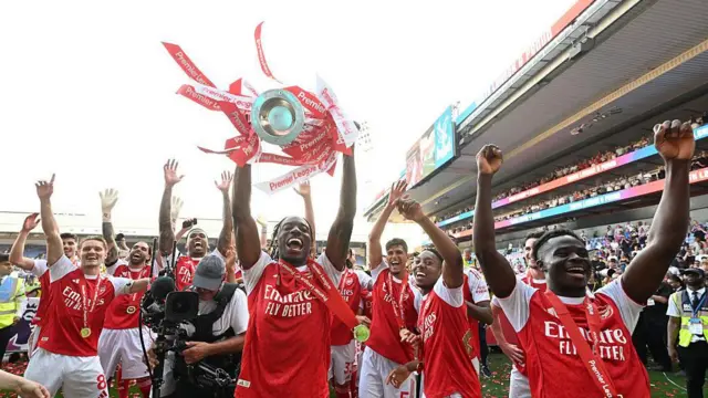 Noni Madueke lifts the Premier League trophy surrounded by his Arsenal team-mates
