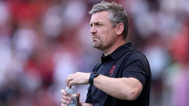 Bristol City boss Michael Skubala in a black short-sleeved polo shirt and holding a bottle of water on the touchline