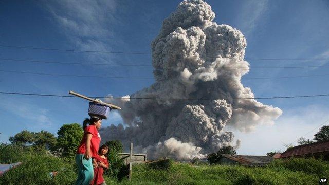 A woman and her daughter walk on a road as Mount Sinabung releases volcanic material into the air in Gamber, North Sumatra, Indonesia,